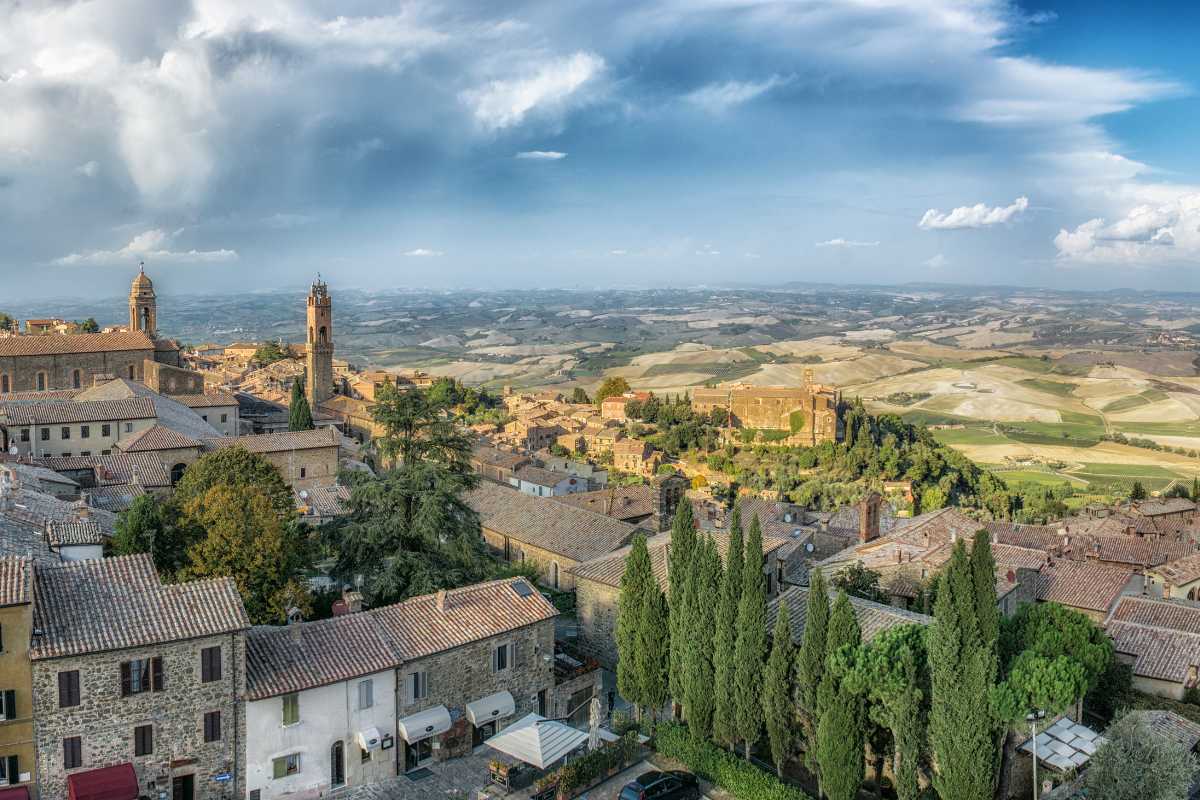 Scorcio panoramico di Montalcino dall’alto, con le sue mura medievali che abbracciano il borgo e la campagna toscana all’orizzonte, luce dorata del pomeriggio