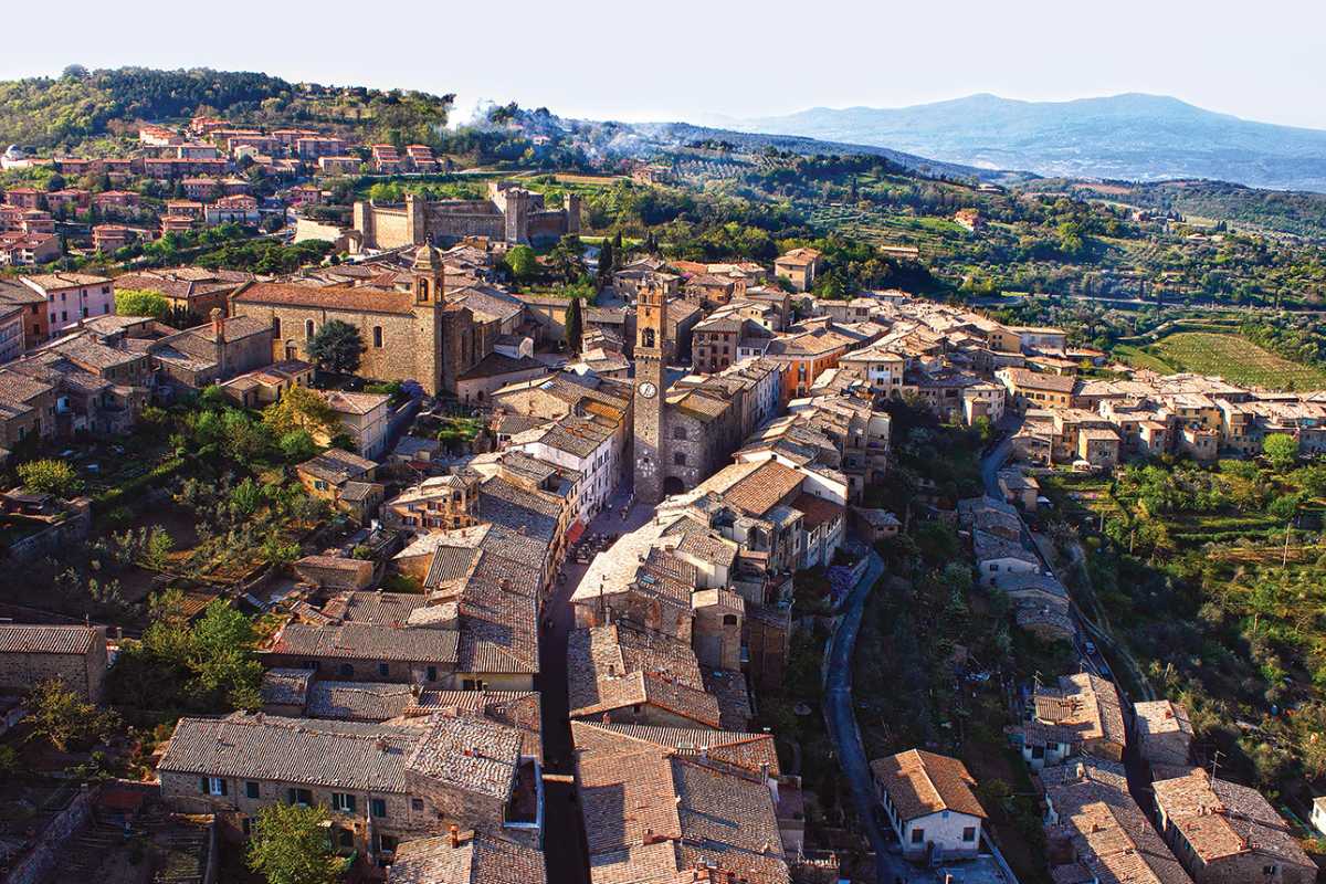 Scorcio di un parco verde di Montalcino con bambini che giocano e gente che passeggia tra gli alberi; sullo sfondo il borgo medievale